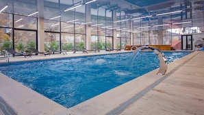 Una piscina interior con paredes de vidrio transparente, sillones de descanso y un diseño moderno de techo.