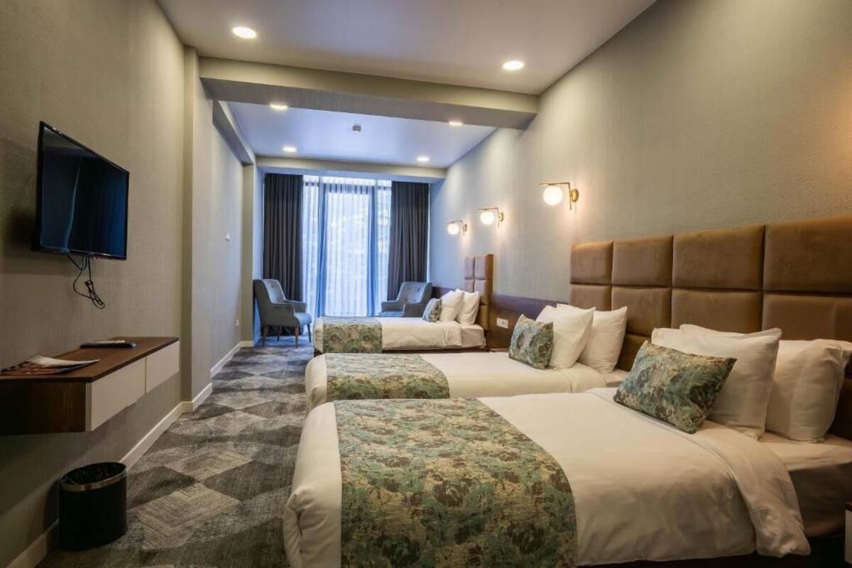 A hotel room with two beds, a TV, a desk, and a view of the city.