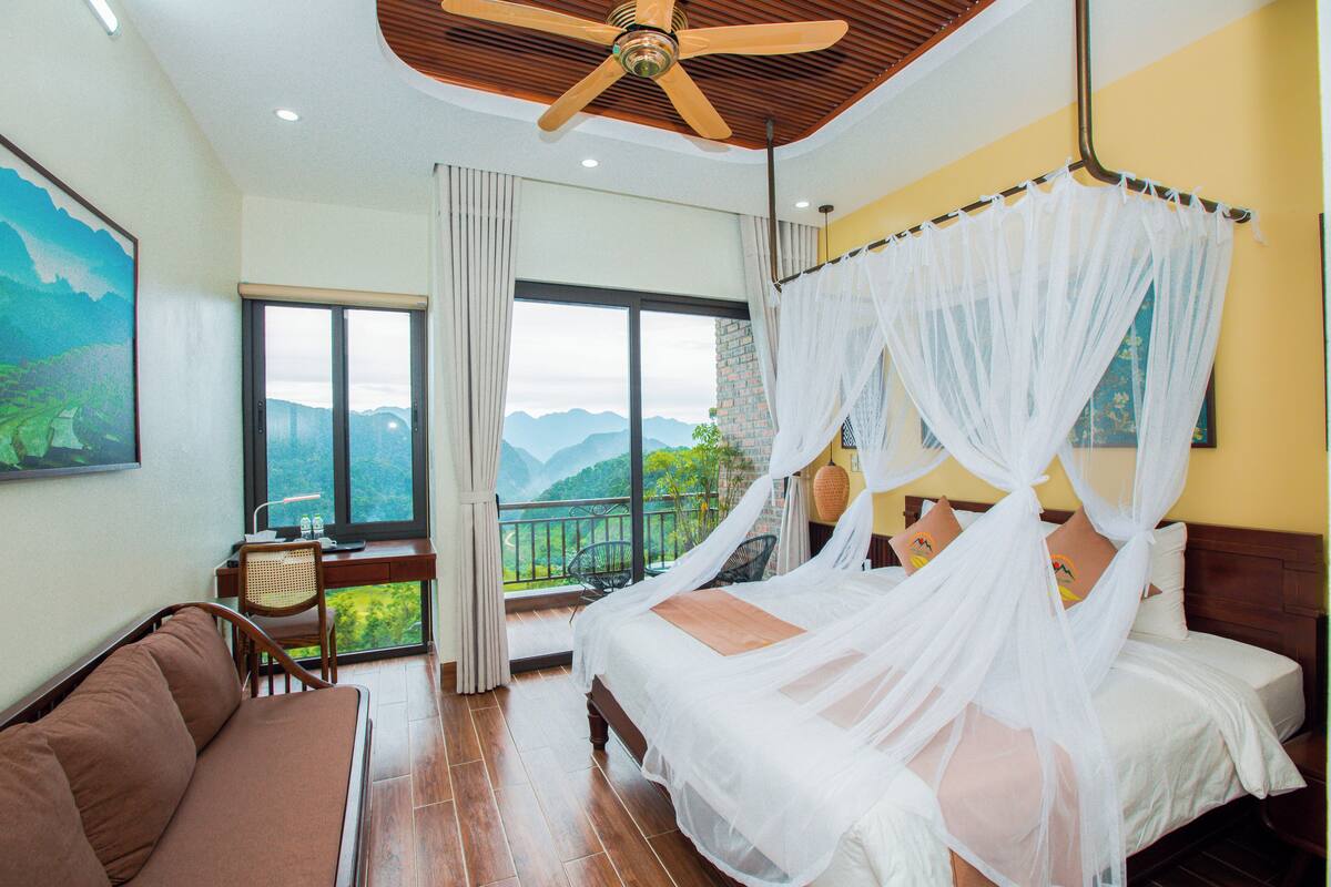 A bedroom with a bed, a sofa, a desk, and a view of mountains.