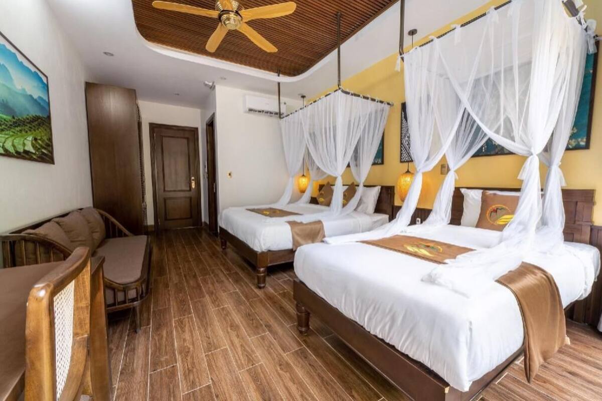 A hotel room with two beds, a ceiling fan, a wooden floor, and a painting on the wall.