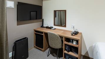 A hotel room with a wooden desk, a chair, a TV, a mirror, a coffee machine, and a minibar.