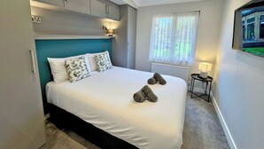 Un dormitorio con cama, mesita de noche, ventana con cortinas, televisor de pared y luz de techo.