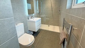 Un baño moderno con inodoro, lavamanos, ducha y un perchero para toallas.
