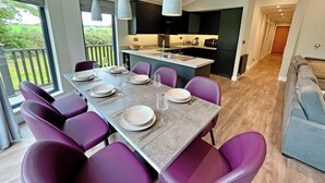 Un comedor moderno con una mesa larga dispuesta para seis comensales, sillas moradas y lámparas colgantes.