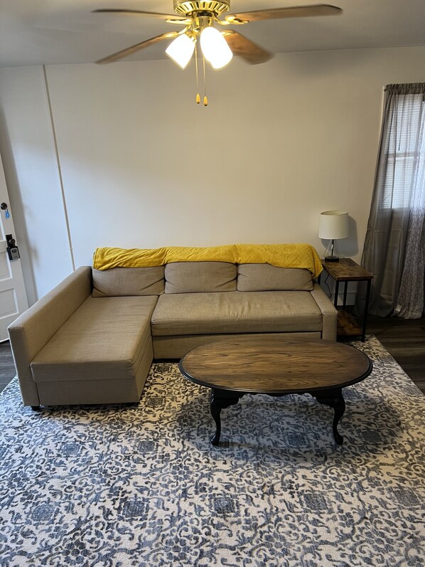A living room with a sectional sofa, a round coffee table, a patterned rug, a ceiling fan, and a lamp on a side table. - Comfy Quiet 1bedroom apartment, close to DT Winslow (Winslow)