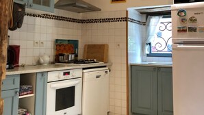 Une cuisine compacte équipée d’une cuisinière à gaz, d’un four et d’un lave-vaisselle, avec des poutres en bois au plafond et un réfrigérateur.