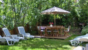 Un espace extérieur aménagé en terrasse, avec une table et des chaises en bois, entouré de fauteuils de jardin à rayures blanches et bleues.