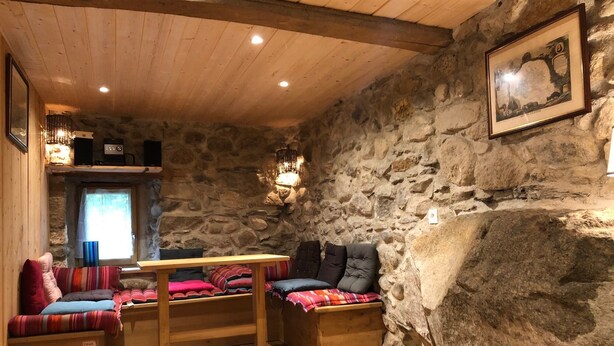 Une pièce chaleureuse aux murs de pierre, meublée de meubles en bois, avec une table et des bancs.