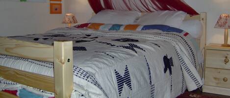 A bed with a white and blue patterned bedspread, a wooden headboard, and a red canopy. There are two bedside tables with lamps and a small wall art piece above the bed.