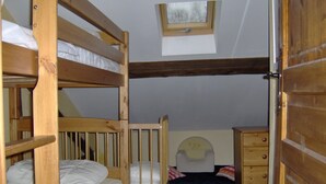 Ein Schlafsaalzimmer mit Etagenbetten, einem kleinen Fenster, einer Kommode und einem Stuhl.