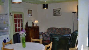 Ein Essbereich mit einem runden Tisch, Stühlen, einer Vase mit Blumen, einem Schrank, einer Couch und einer Stehlampe.