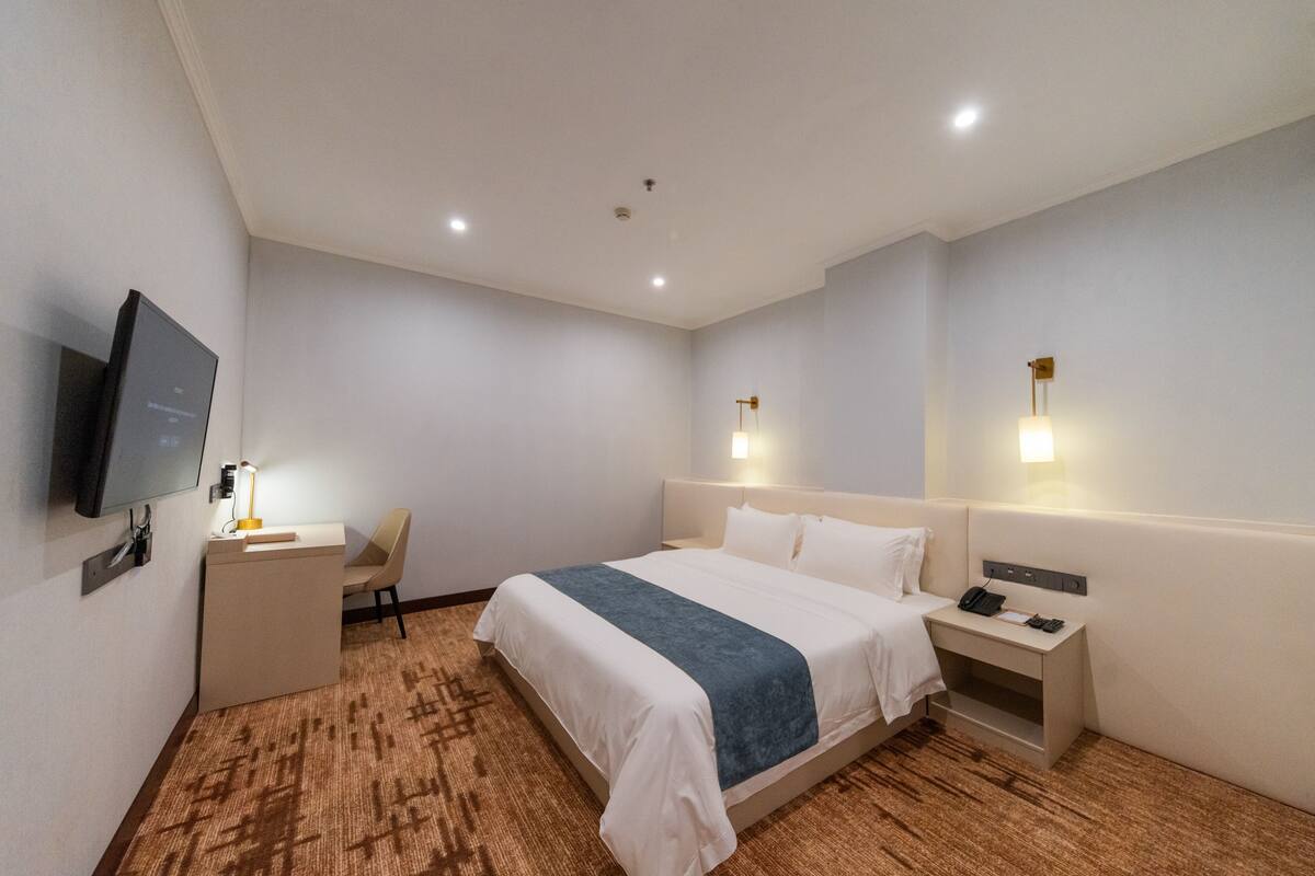 Ein Hotelzimmer mit Bett, Nachttisch, Stuhl, Schreibtisch, Fernseher und Wandlampen.