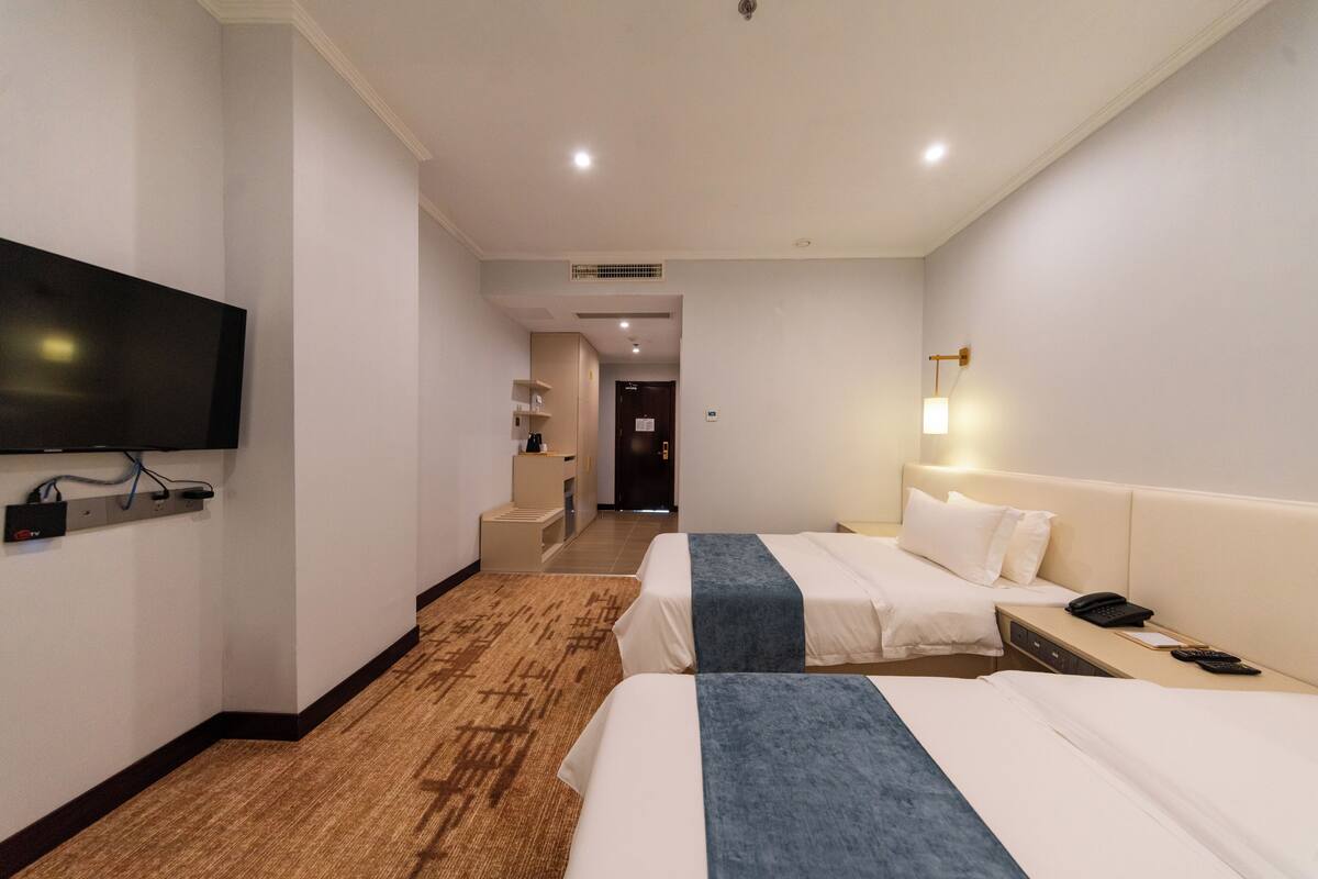 Ein Hotelzimmer mit zwei Betten, einem Fernseher, einem Schreibtisch mit Telefon und Teppichboden.