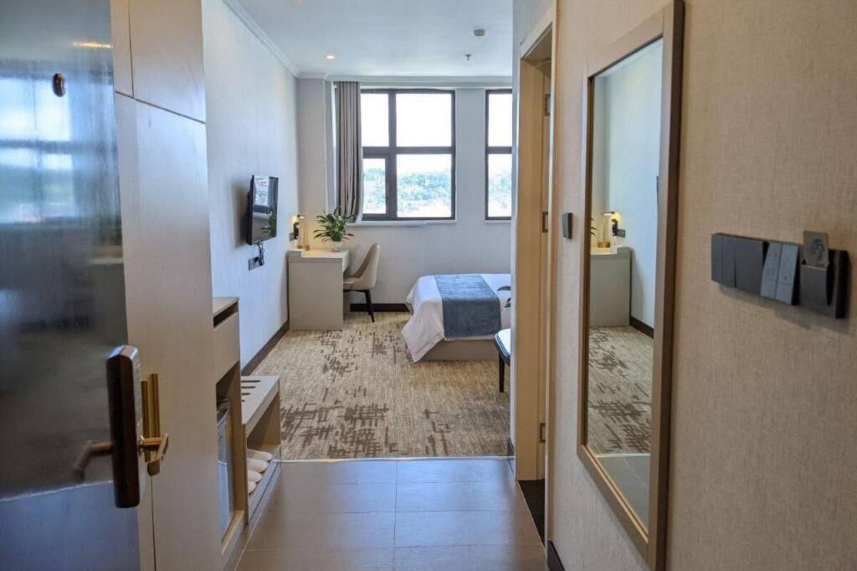Ein Hotelzimmer mit Bett, Nachttisch, kleinem Schreibtisch mit Stuhl, Fenster und Spiegel an der Wand.