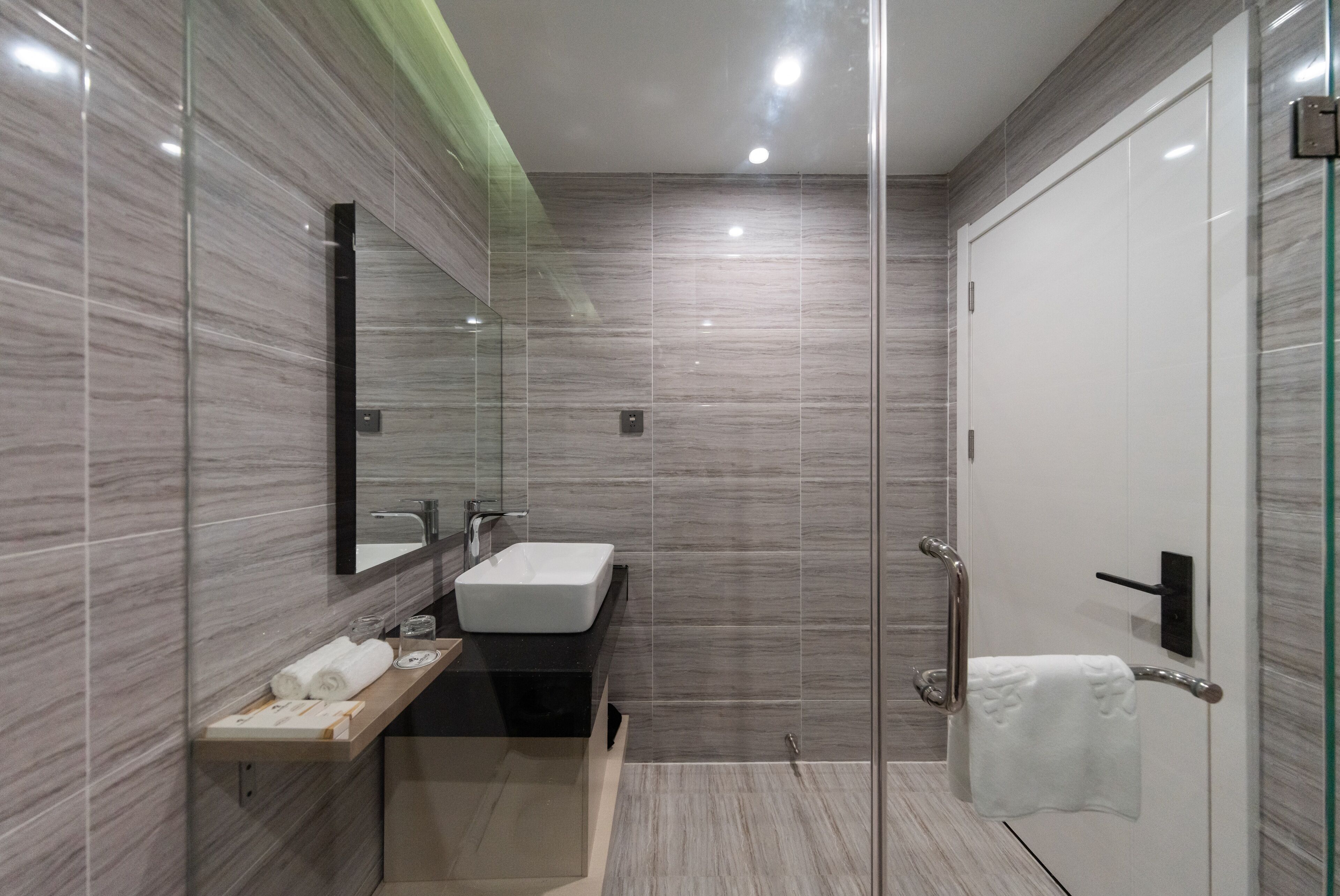 Un bany modern amb plat de dutxa de vidre, un lavabo blanc i un suport per a tovalloles.