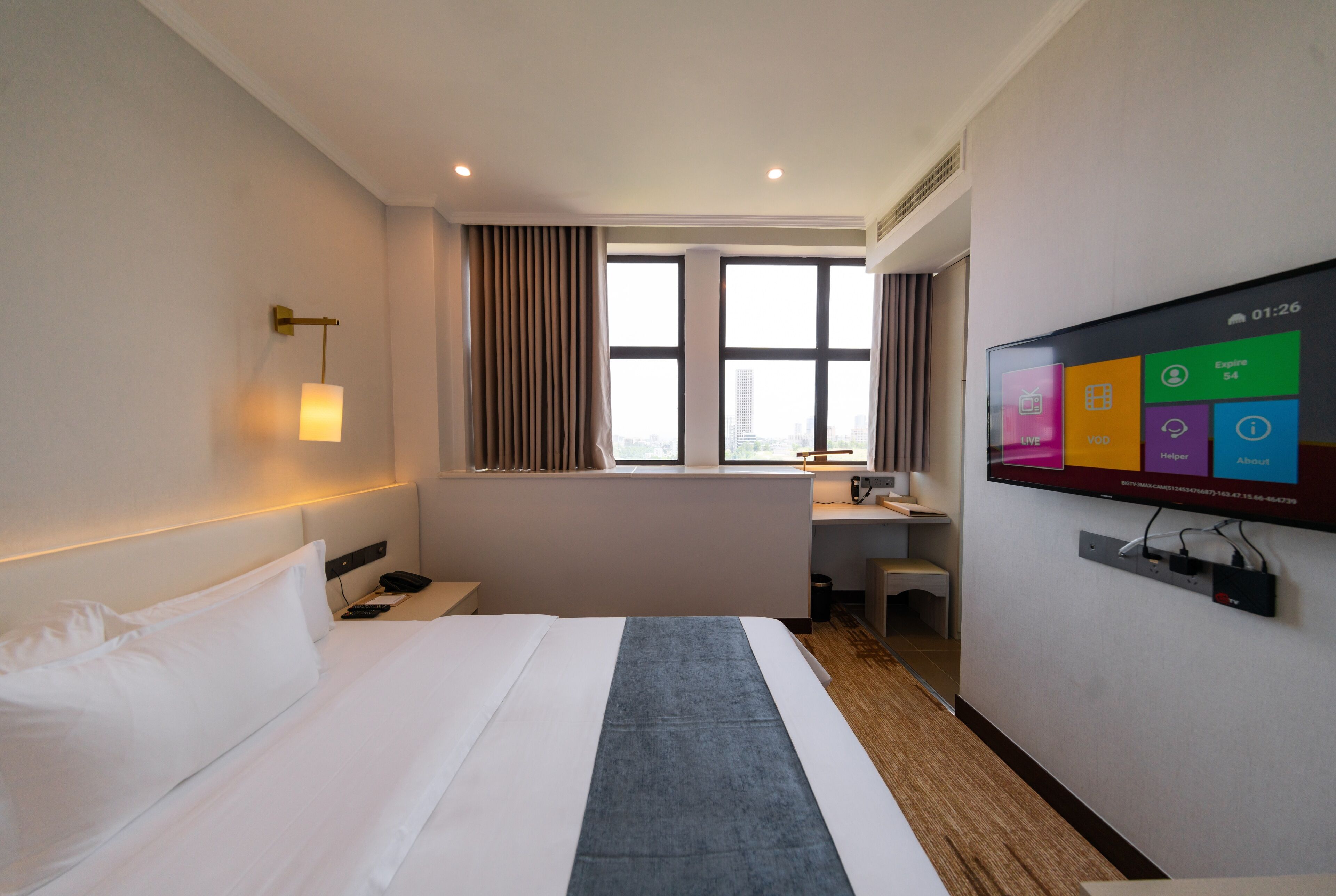 A hotel room with a bed, a desk, a TV, and a window with curtains.