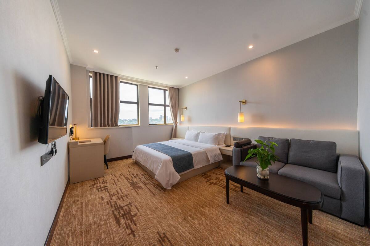 Ein Hotelzimmer mit Bett, Sofa, Fernseher, Schreibtisch und einem Fenster mit Vorhängen.