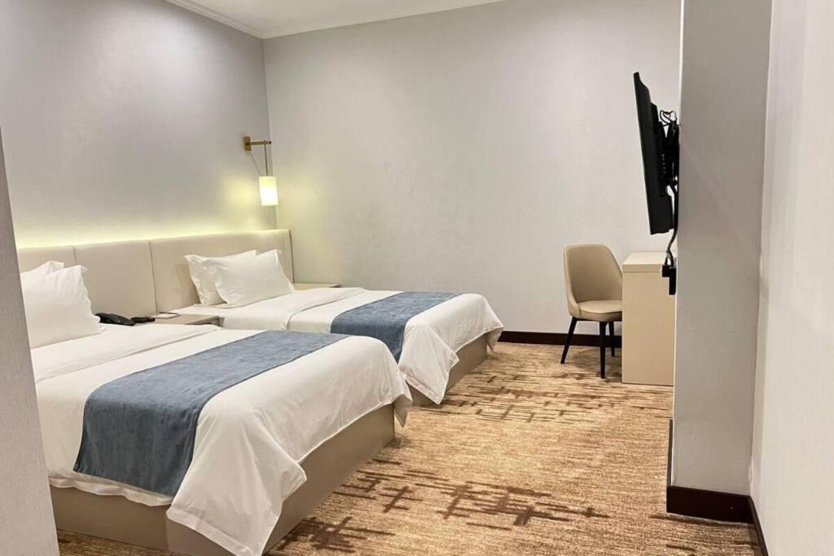 Ein Hotelzimmer mit zwei Betten, einem Schreibtisch, einem Stuhl und einem Fernseher.