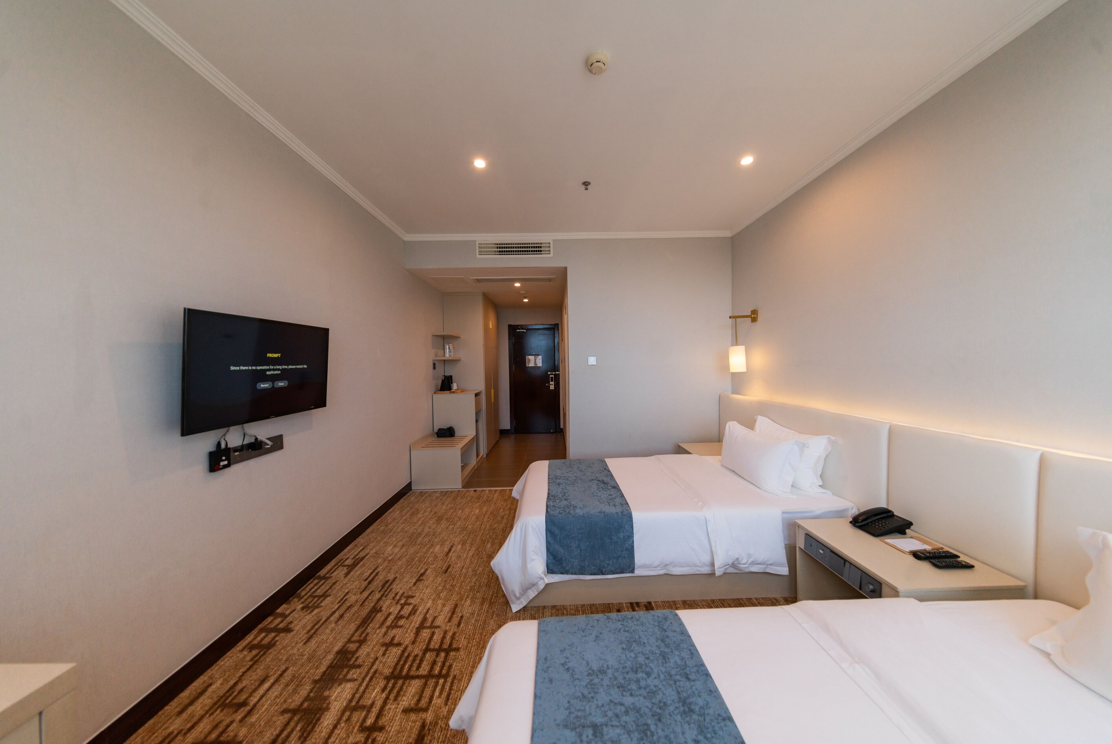 A hotel room with two beds, a TV, a desk with a phone, and a lamp.