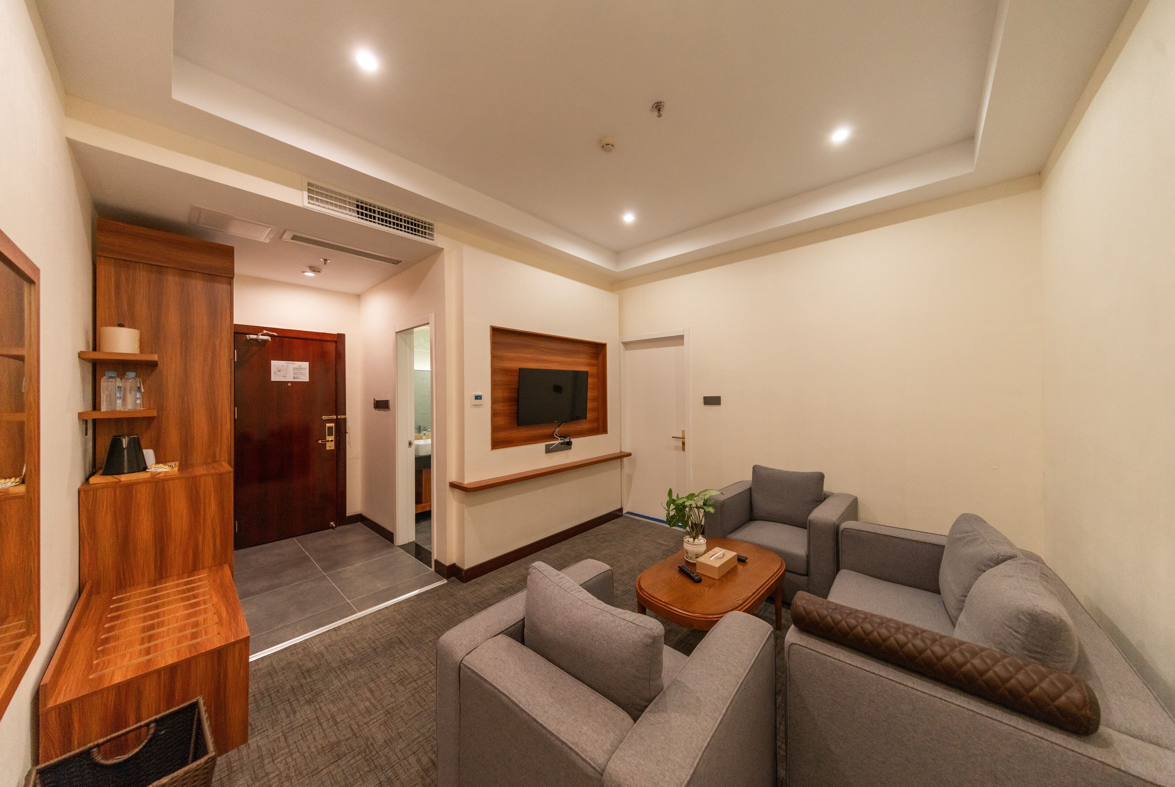 A modern living room with a grey sofa set, a wooden coffee table, and a flat-screen TV mounted on the wall.