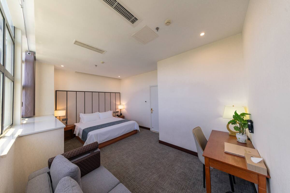 Ein Hotelzimmer mit Bett, Schreibtisch, Stuhl, Sofa und Fenster.