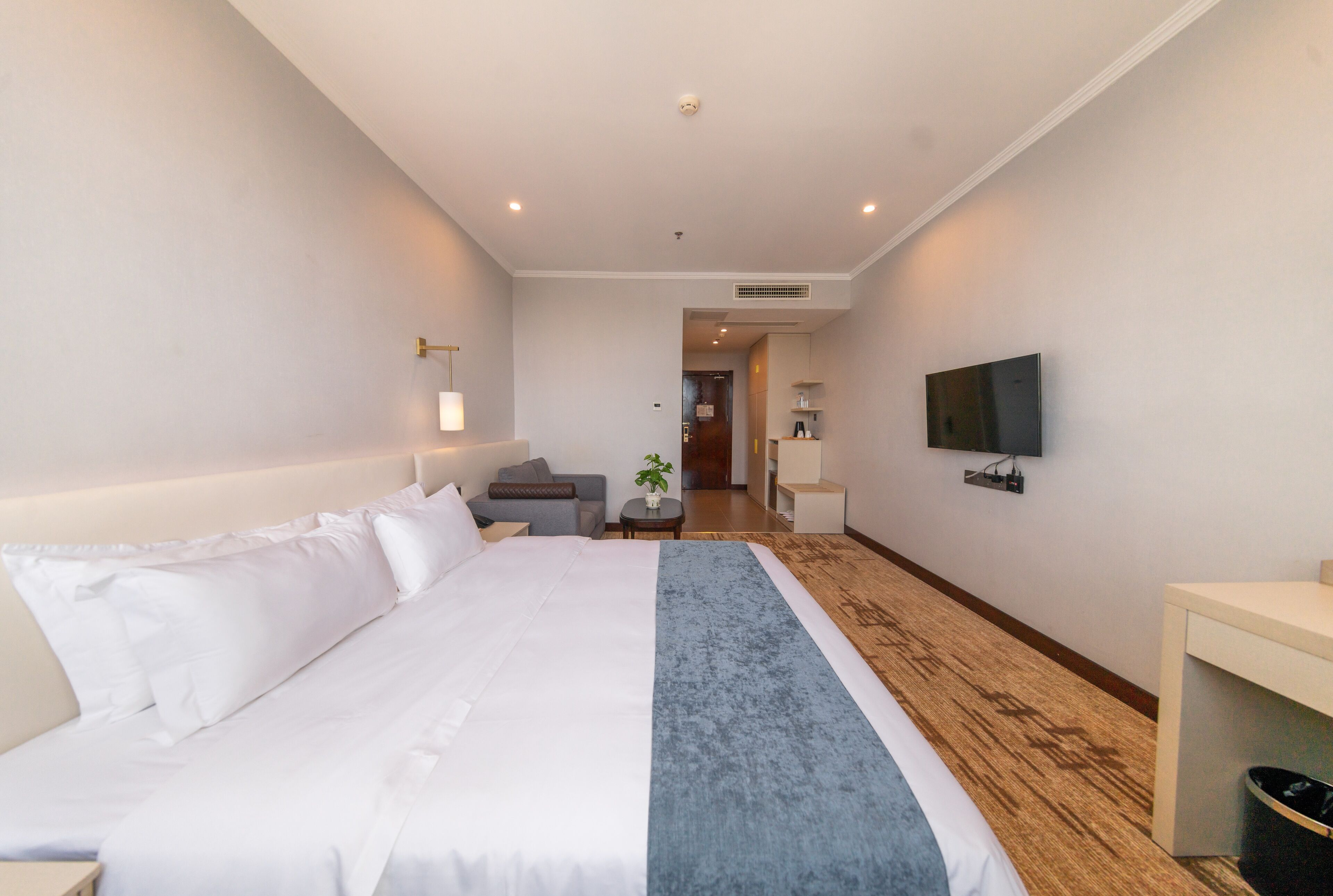 Quarto de hotel com uma cama grande, televisão fixada na parede e uma pequena escrivaninha com cadeira.