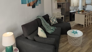 Un soggiorno moderno con un divano, un tavolino rotondo e una lampada. È presente una zona cucina con frigorifero, microonde e tavolo da pranzo.
