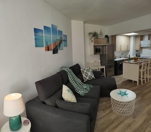 A modern living room with a sofa, a small round table, and a lamp. There is a kitchen area with a refrigerator, microwave, and a dining table. - Renovated apartment in central Torremolinos with Wi-Fi and air conditioning (Torremolinos)