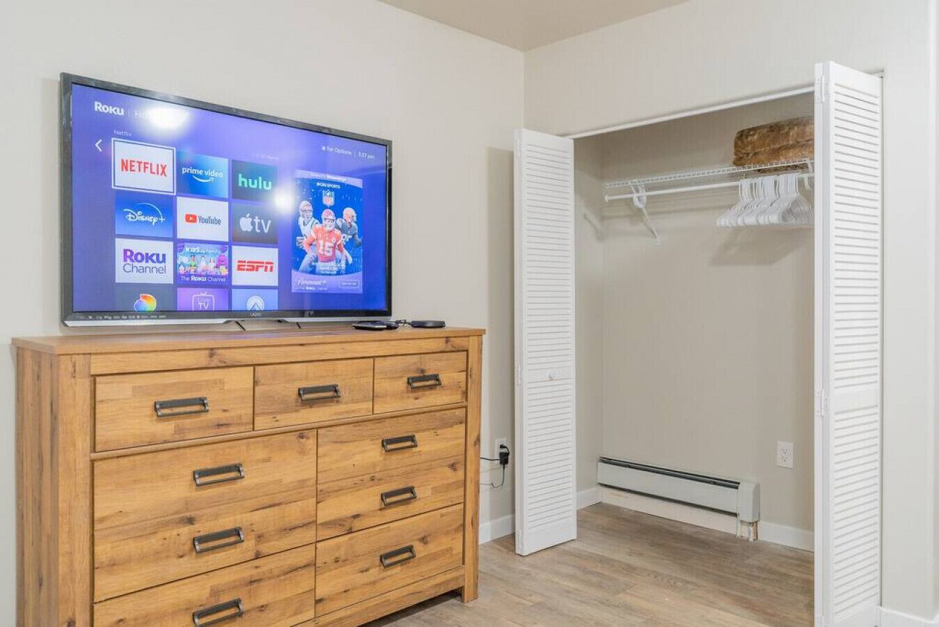 Habitació amb televisió que mostra diverses plataformes de streaming, un taulell de nit de fusta i un armari amb portes aclapades blanques.