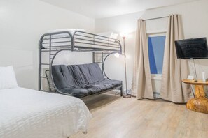 A bunk bed with a desk and chair, a television, and a window with curtains.