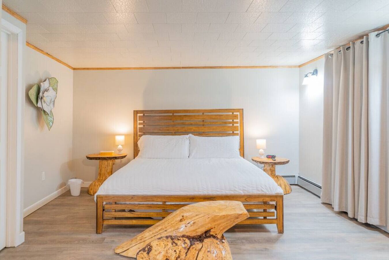 Une chambre à coucher avec un lit en bois, deux tables de chevet, une petite table, un banc en bois et une lampe fixée au mur.