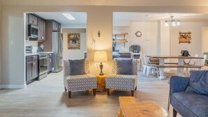 Una sala de estar moderna con dos sillones estampados, una mesa de centro de madera y una zona de comedor con mesa y sillas.