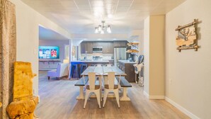 Una cocina moderna con una isla central, un comedor con mesa y sillas, y una sala de estar con televisor.