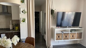 Una cucina moderna con zona pranzo, una TV su un mobile bianco e un corridoio che conduce ad altre stanze.