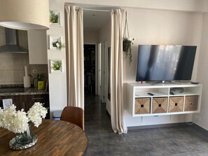 A modern kitchen with a dining area, a TV on a white stand, and a hallway leading to other rooms. - Stunning 3BR Apartment in Torremolinos with Balcony Near Beaches and Plaza Andalucia (Torremolinos)