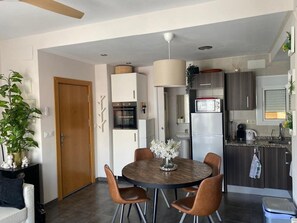 A modern kitchen with white cabinets, a built-in oven, a microwave, and a refrigerator. There is a dining table with chairs and a vase of flowers. - Stunning 3BR Apartment in Torremolinos with Balcony Near Beaches and Plaza Andalucia (Torremolinos)