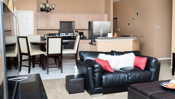 Ein modernes Wohnzimmer mit einer schwarzen Ledersofa, einem Essbereich mit Stühlen, einer Küche mit Kühlschrank und einer Kristallleuchtre.