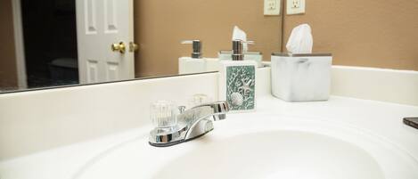 A bathroom with a white sink, chrome faucet, and a mirror reflecting a door and wall outlets.
