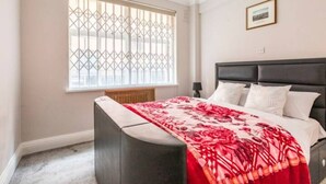 Una camera da letto con un letto, un comodino, una finestra con zanzariera e un quadro appeso al muro.