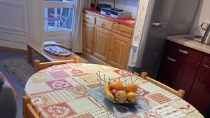 A dining area with a round table covered by a patterned tablecloth, wooden chairs, and a fruit bowl on the table. - Superb 32 m2 apartment with GARAGE and slope view (VARS)