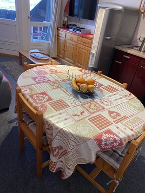 A dining area with a round table covered by a patterned tablecloth, wooden chairs, and a fruit bowl on the table.