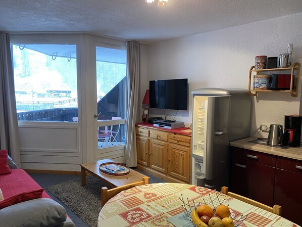 A compact living space with a dining area, kitchenette, and a television.