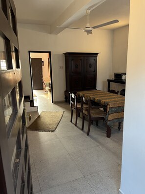 Una habitación con una mesa de comedor, sillas, un armario de madera oscura, un ventilador de techo y una puerta que da a otra habitación.
