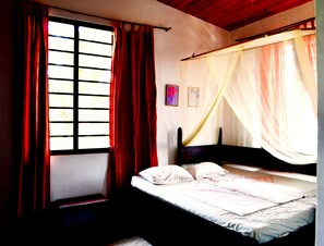Une chambre à coucher avec un lit, une fenêtre avec des rideaux et une moustiquaire.