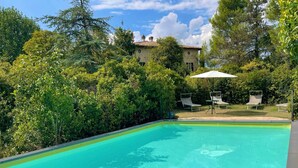 Una piscina cristalina rodeada de exuberante vegetación y un edificio de piedra al fondo.