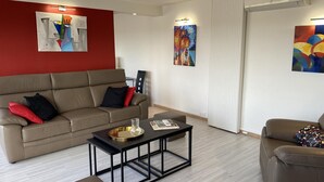 Un salon moderne avec un canapé beige, une table basse et deux fauteuils. On y trouve trois œuvres d’art murales et une porte coulissante.