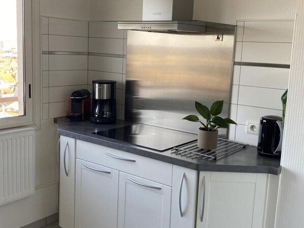 Une cuisine moderne avec des meubles blancs, une hotte en acier inoxydable, une machine à café et une plante en pot.