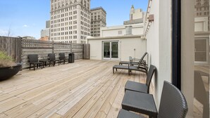 A rooftop patio with wooden flooring, outdoor seating, and a view of city buildings. - Modern 1BR Downtown condo with rooftop gym & skyline views. King bed, Wi-Fi, walk to Canal & FQ (New Orleans)