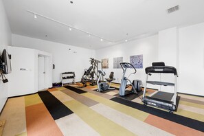 Ein Fitnessstudio mit unterschiedlichen Trainingsgeräten, einem gemusterten Teppich und weißen Wänden.