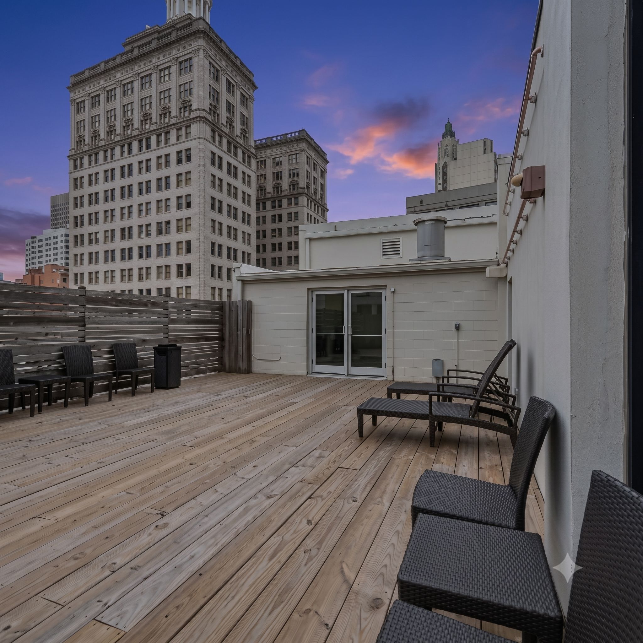 Une terrasse sur le toit, dotée d’un plancher en bois, d’un espace salon extérieur et offrant une vue sur un bâtiment historique.